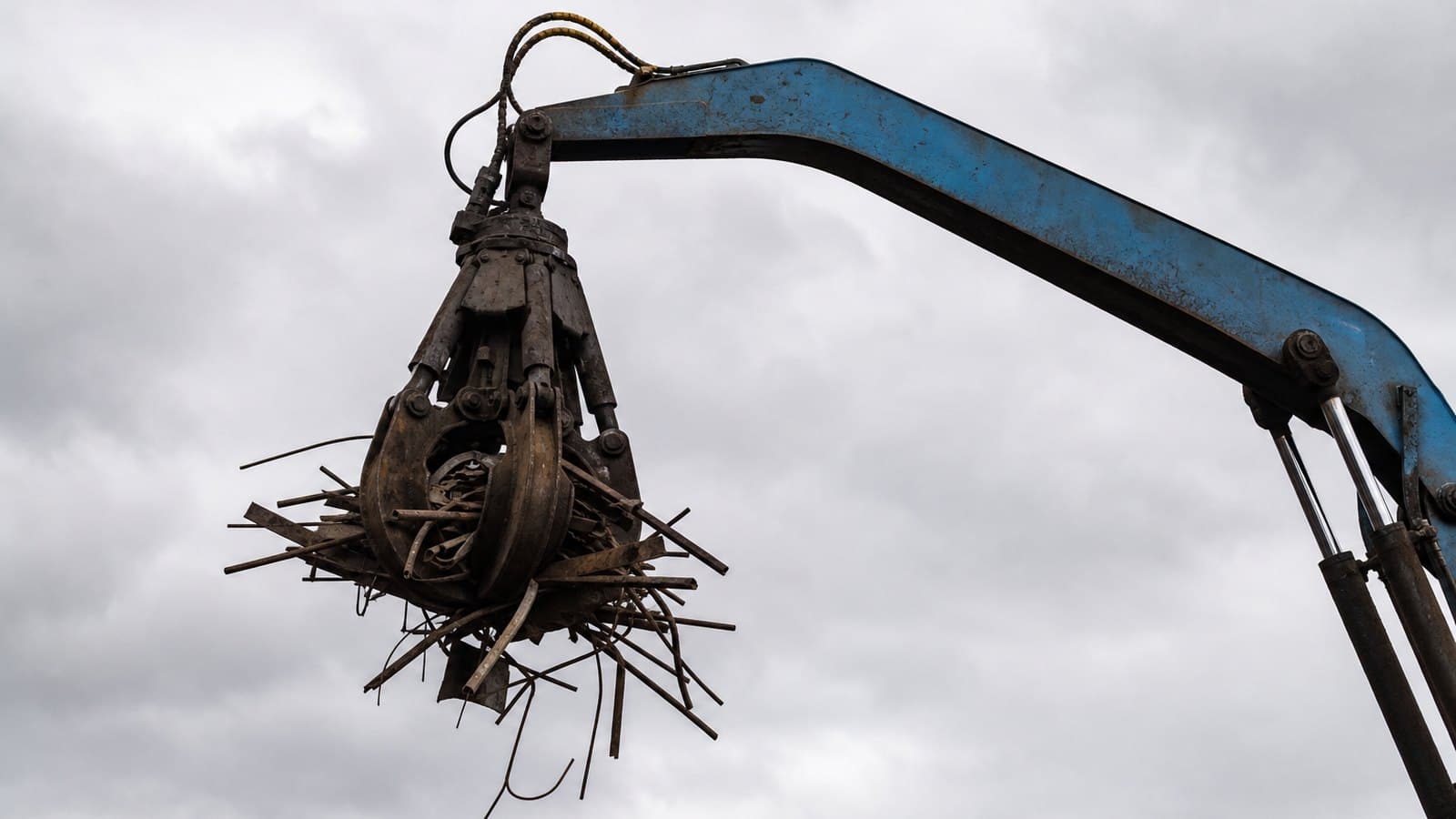 A hydraulic crane arm and grab lifting a bundle of scrap steel