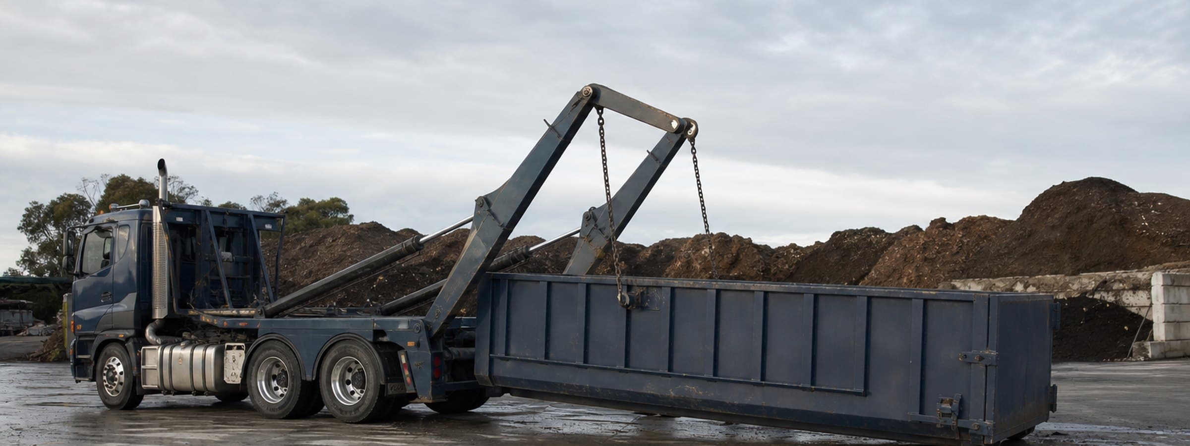 A hook-lift truck lowering a roll-off bin onto a commercial site